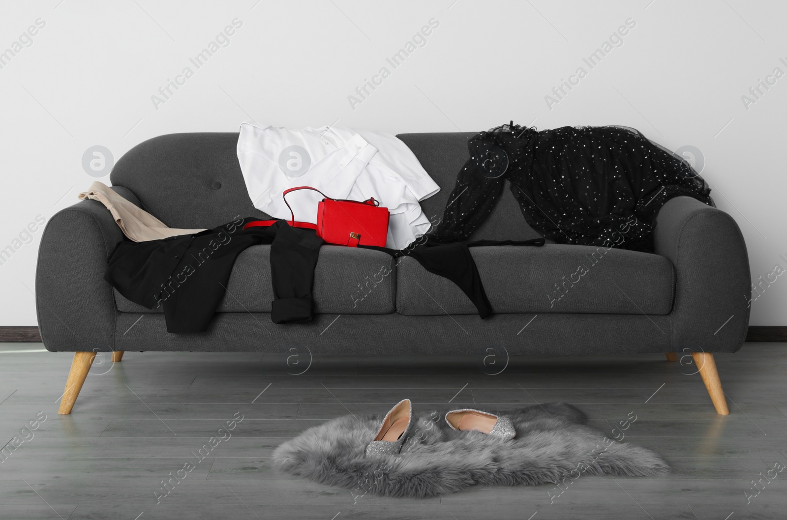 Photo of Messy pile of clothes on sofa and shoes in living room