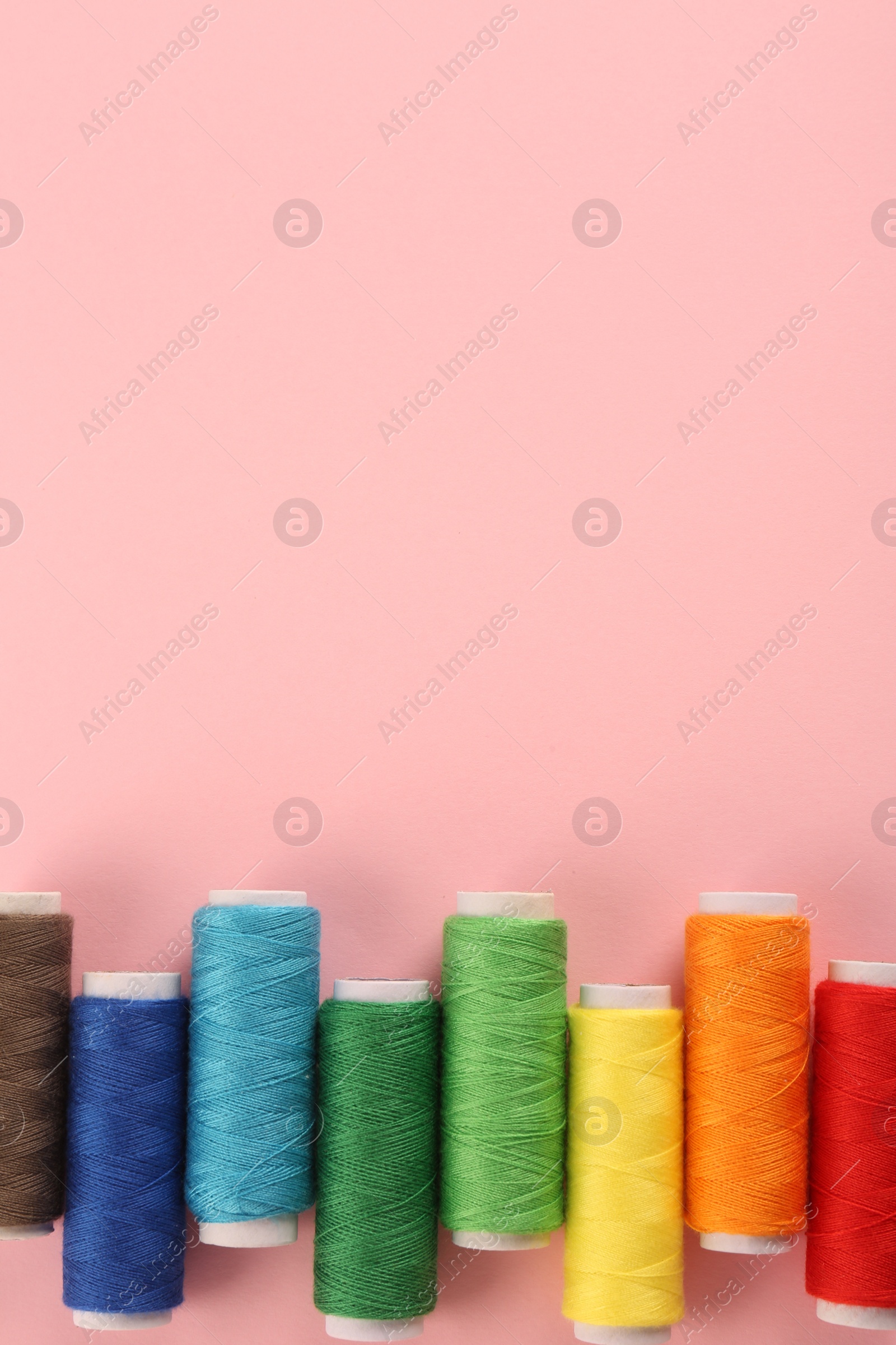 Photo of Different colorful sewing threads on pink background, flat lay. Space for text