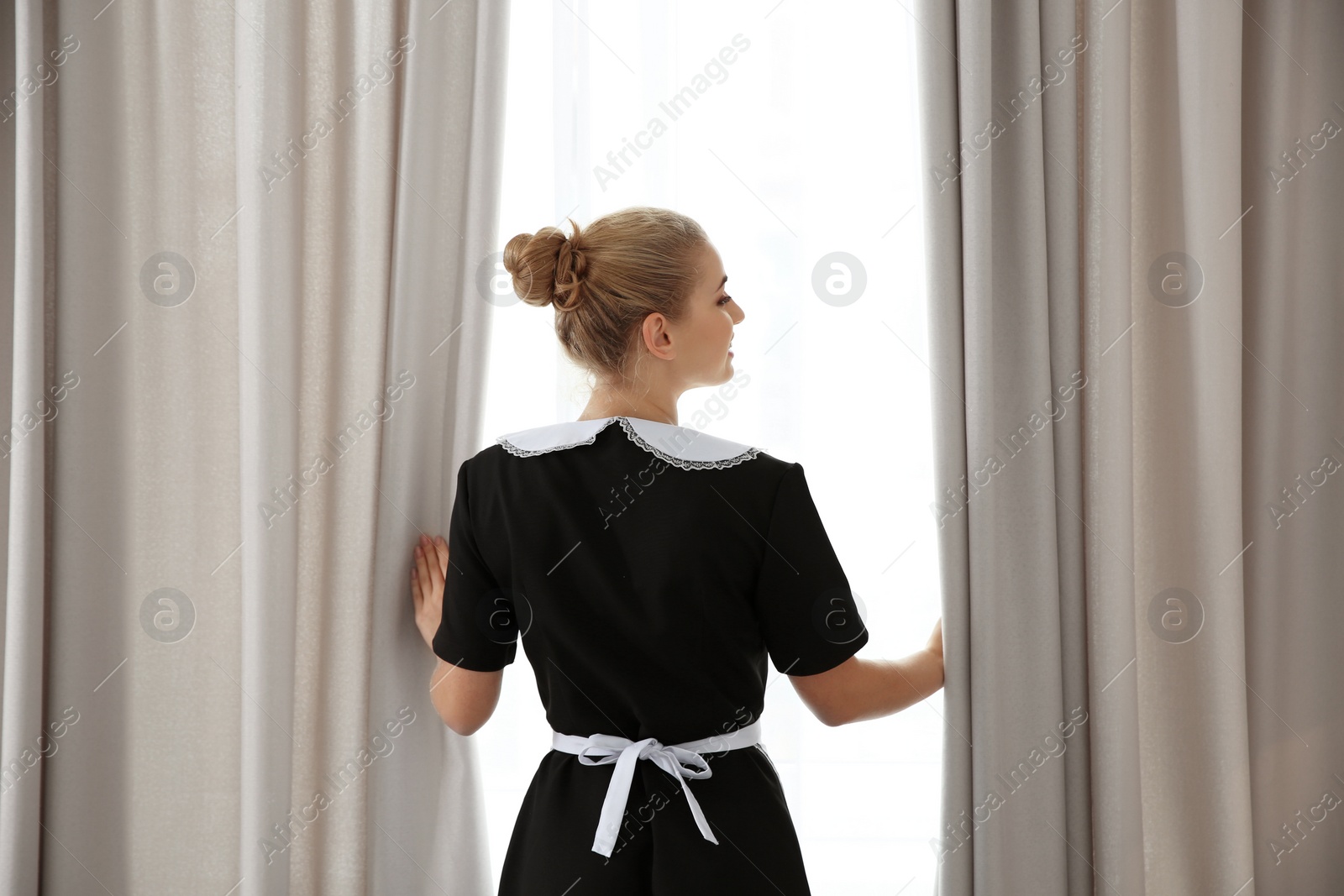 Photo of Young maid opening curtains in hotel room