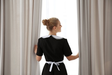 Young maid opening curtains in hotel room