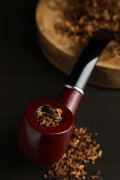 Photo of Smoking pipe and dry tobacco on dark wooden table, closeup