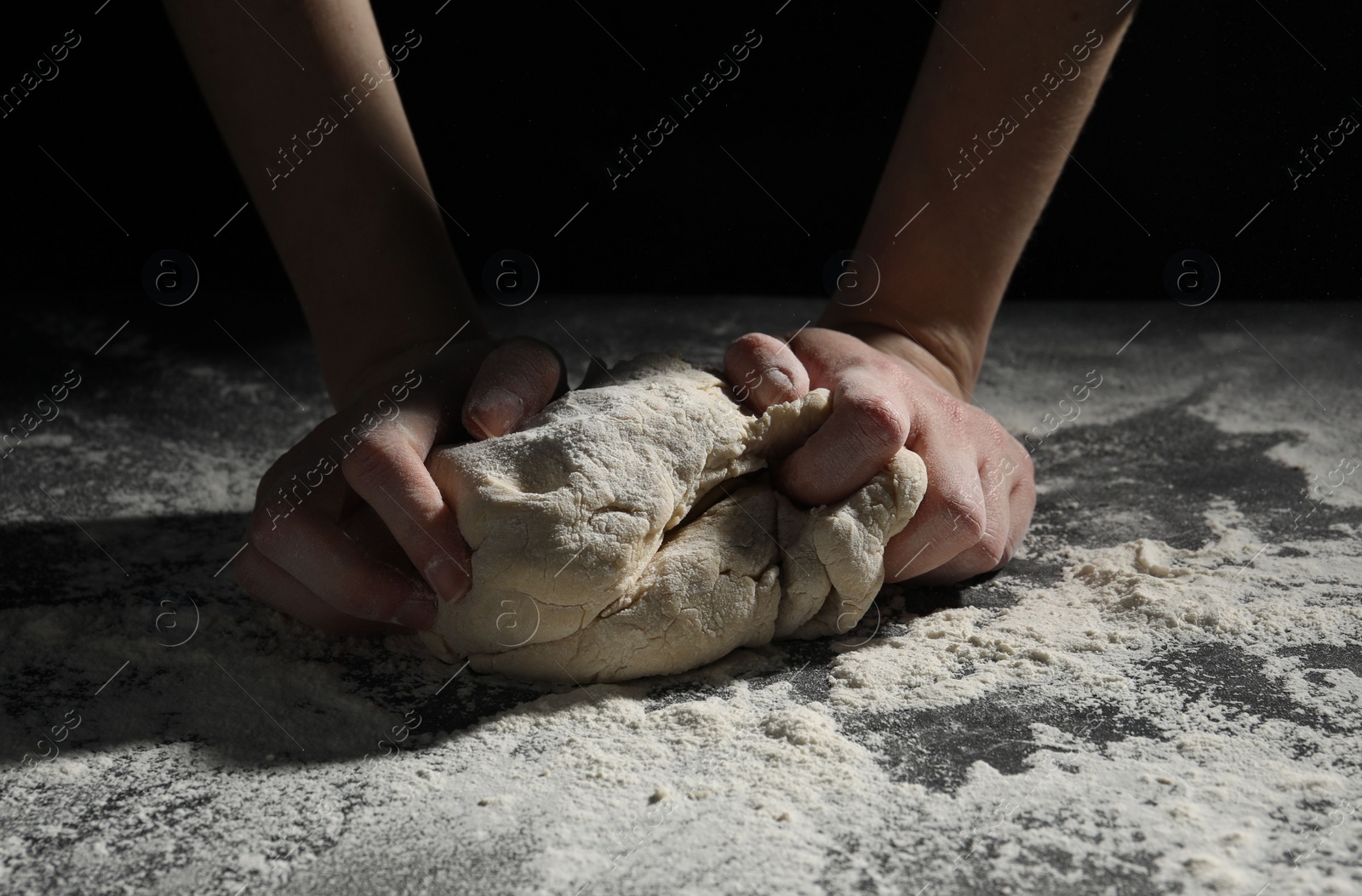 Photo of Making bread. Woman kneading dough at table on dark background, closeup