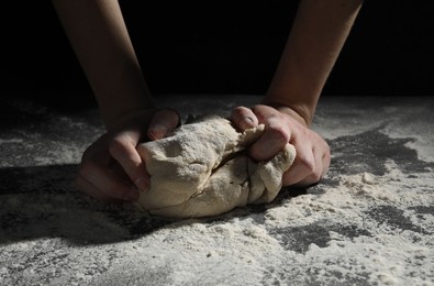 Making bread. Woman kneading dough at table on dark background, closeup