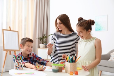 Young woman and children having fun with paints at table indoors