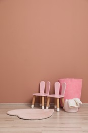 Child's chairs and baskets near pink wall indoors. Interior design