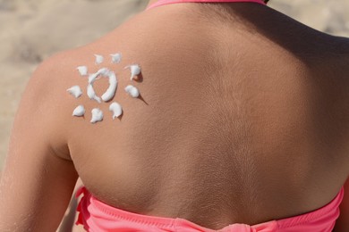 Photo of Little girl with sun protection cream on body outdoors, closeup