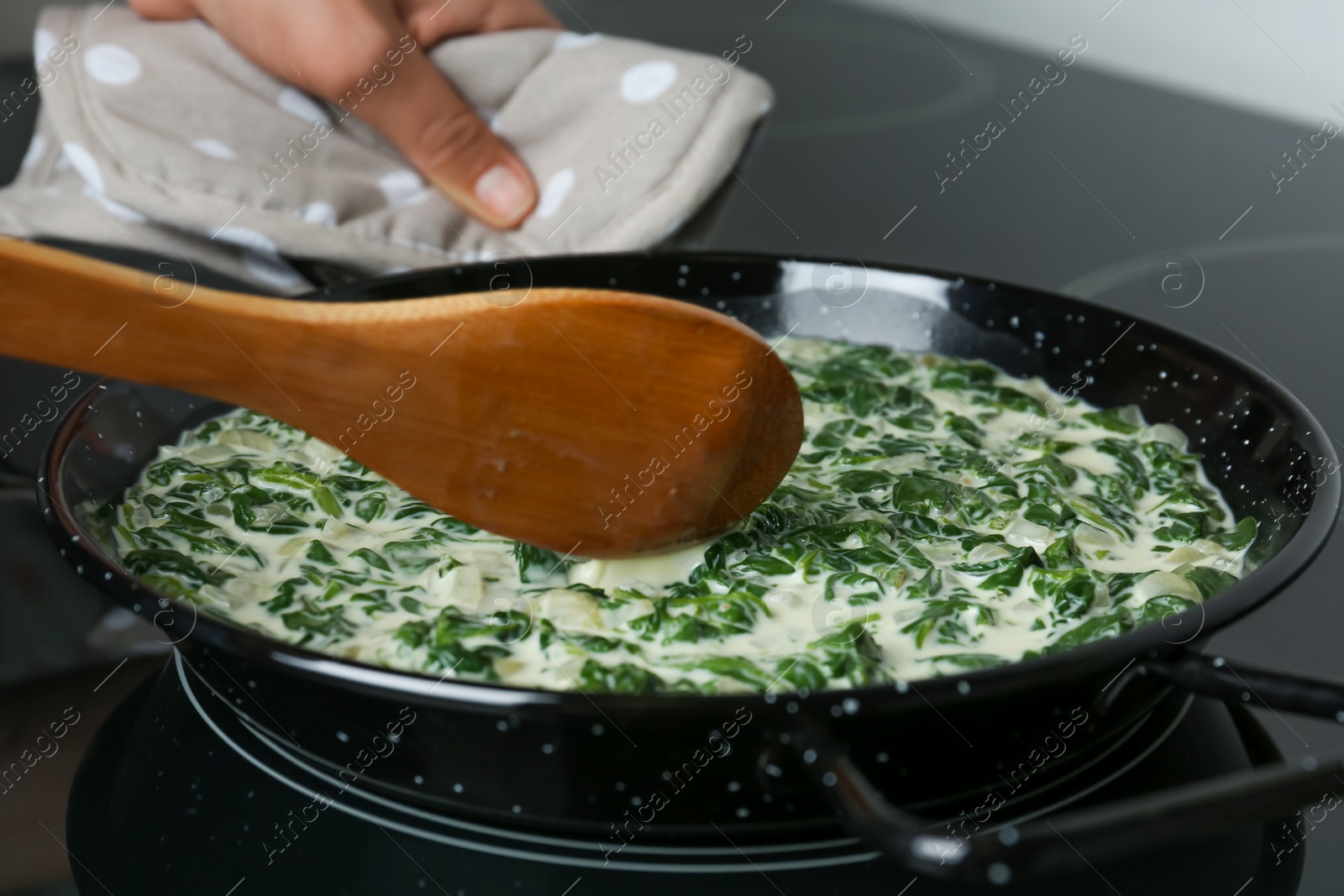 Photo of Woman cooking tasty spinach dip on kitchen stove, closeup view