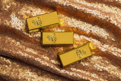 Many shiny gold bars on bronze sequin fabric, flat lay