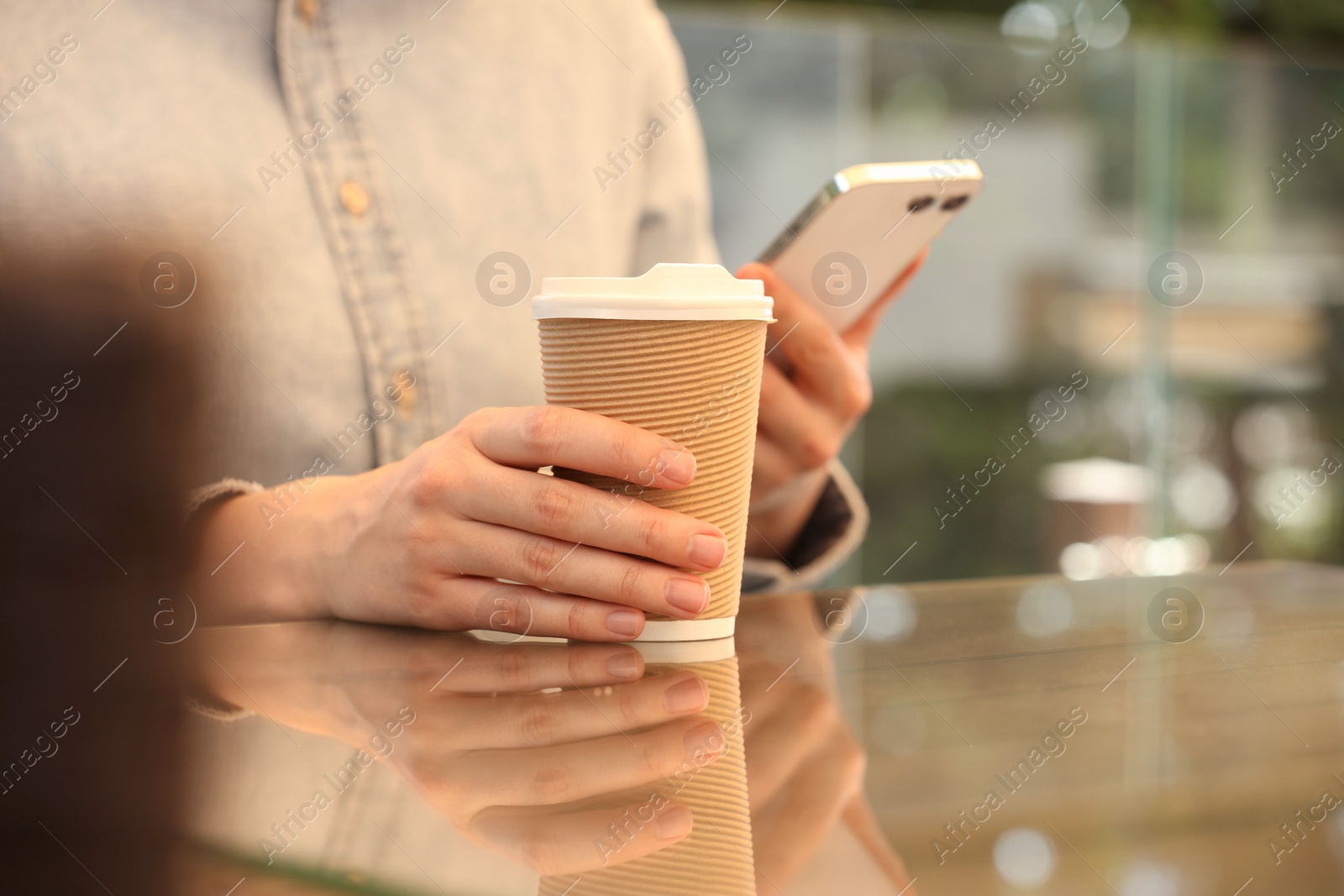 Photo of Woman holding takeaway paper cup and smartphone at table, closeup. Coffee to go