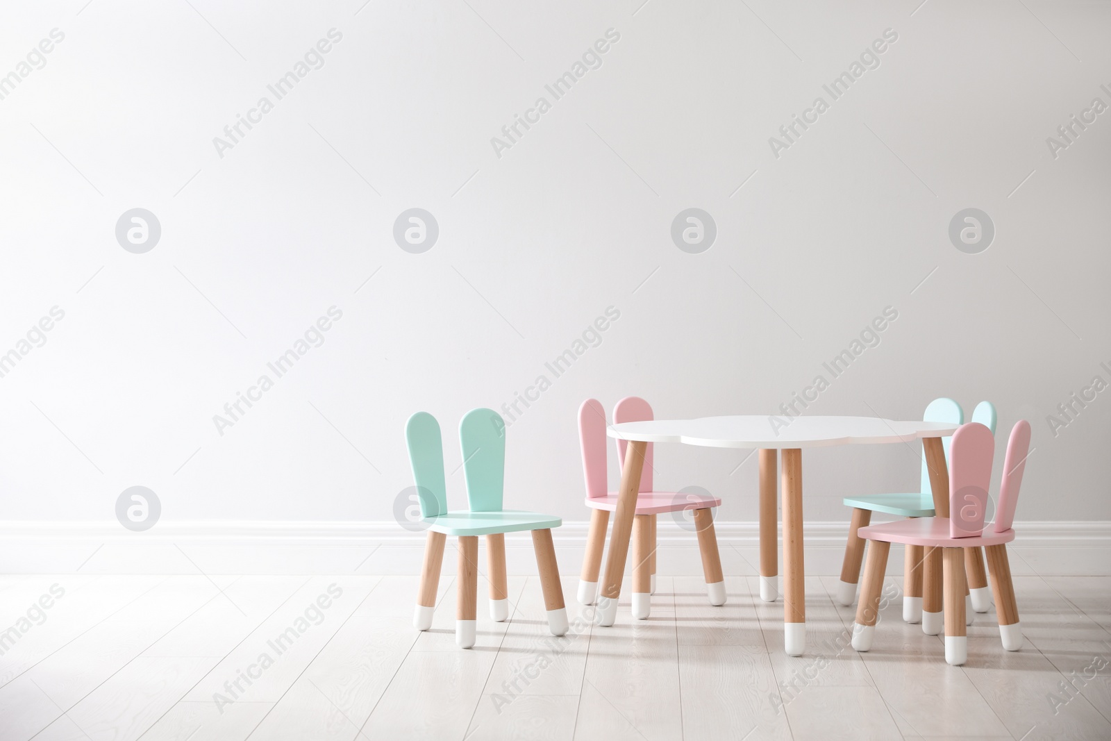 Photo of Small table and chairs with bunny ears near white wall indoors, space for text. Children's room interior