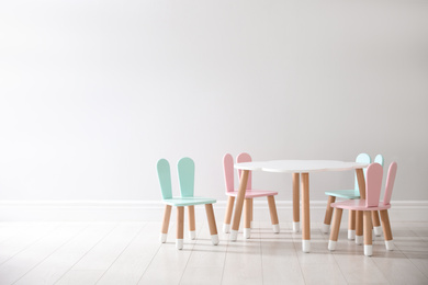 Small table and chairs with bunny ears near white wall indoors, space for text. Children's room interior