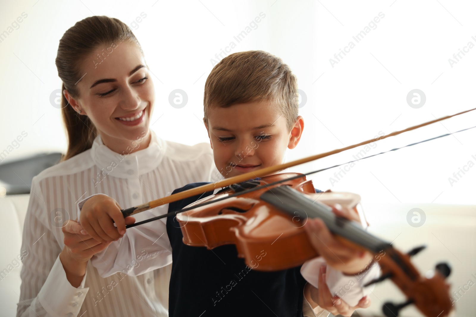 Photo of Young woman teaching little boy to play violin indoors