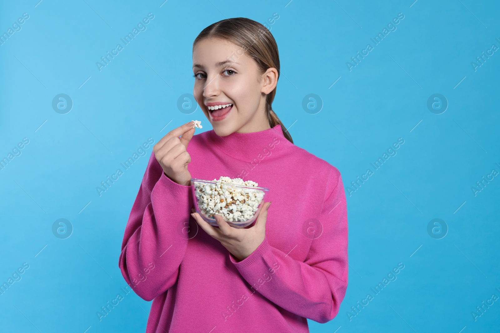 Photo of Teenage girl eating delicious popcorn on light blue background