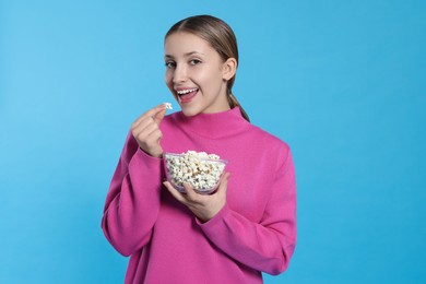 Teenage girl eating delicious popcorn on light blue background