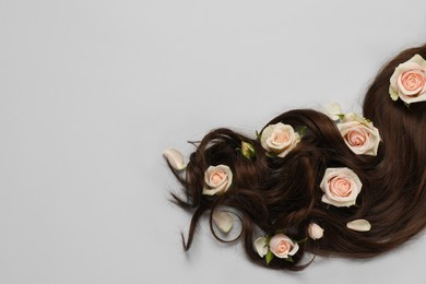 Lock of healthy brown hair with flowers on light grey background, flat lay. Space for text