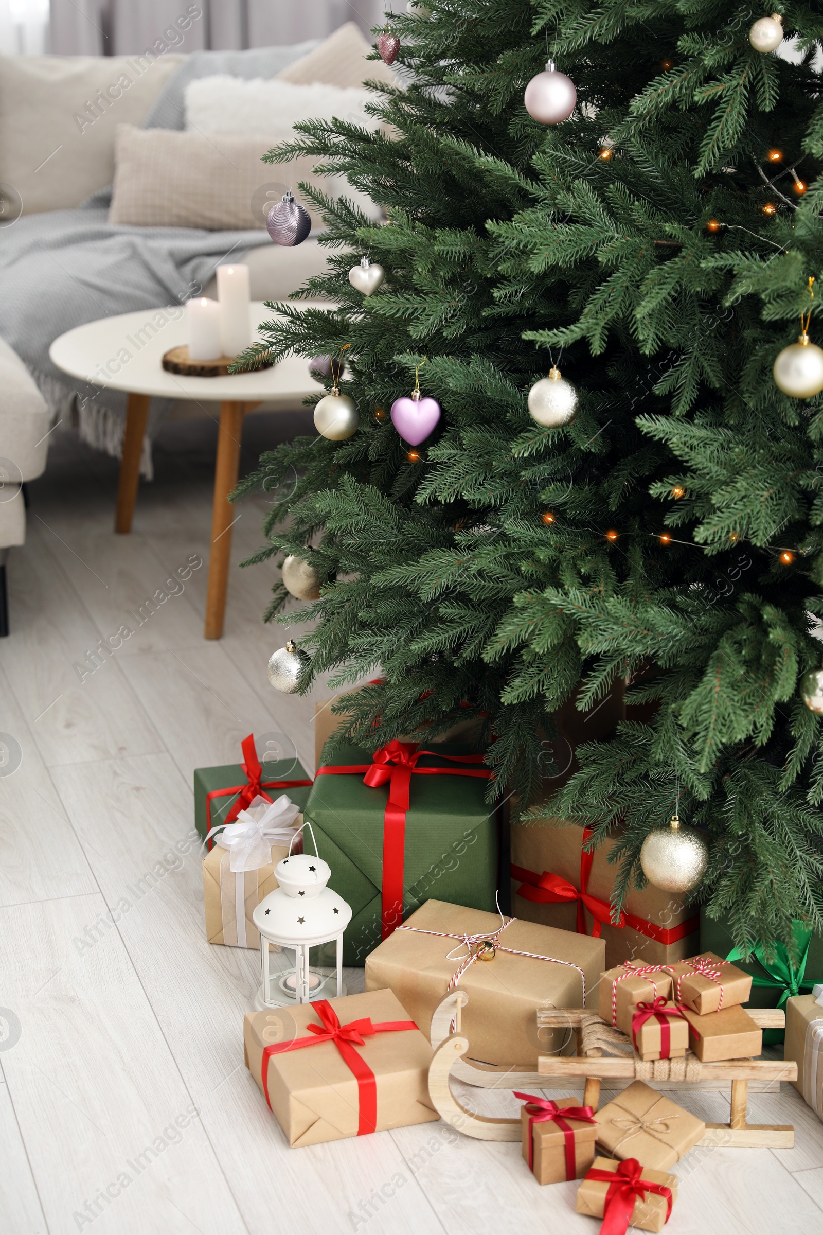 Photo of Beautifully wrapped gift boxes, wooden sleigh and lantern under Christmas tree indoors