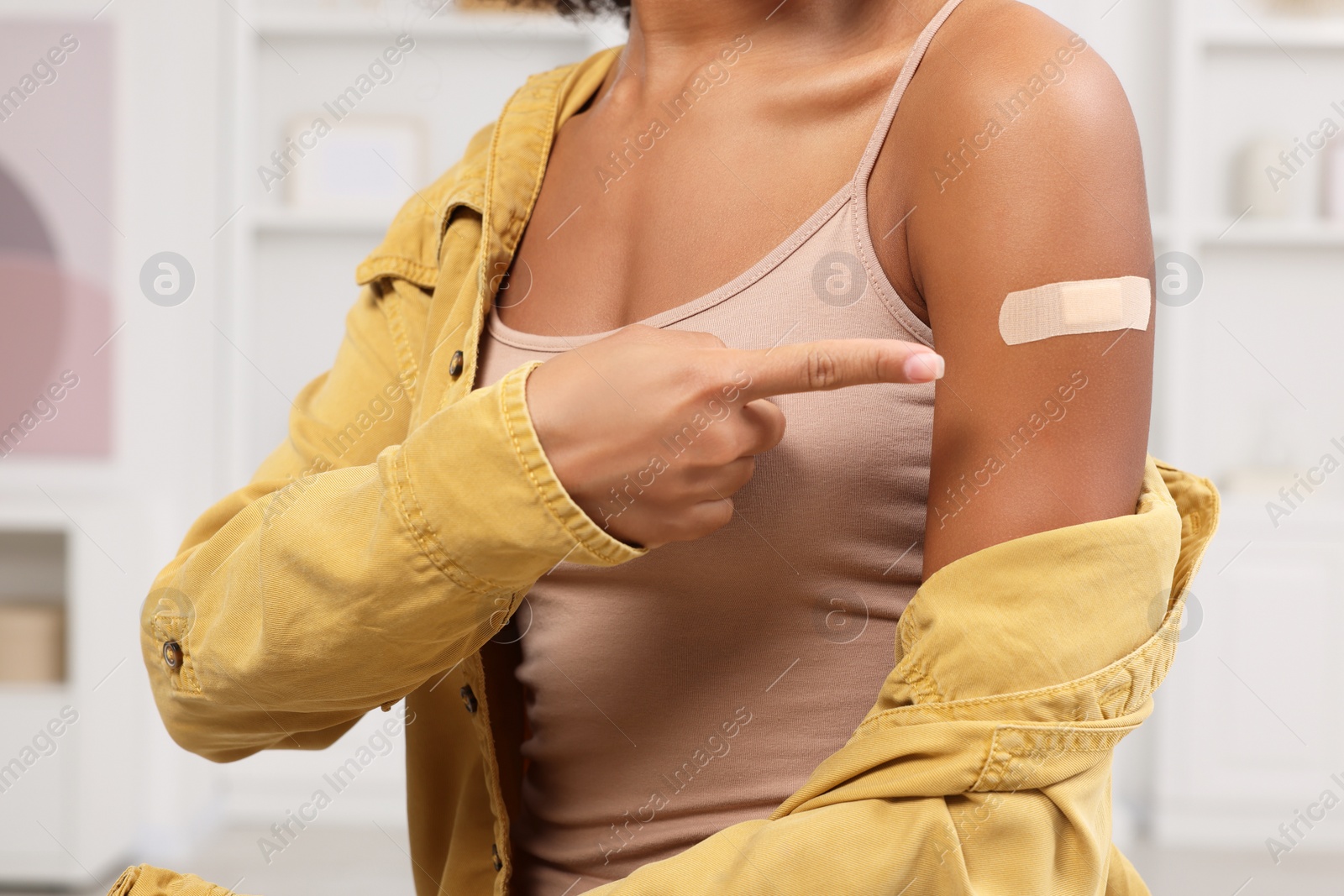 Photo of Young woman pointing at adhesive bandage after vaccination indoors, closeup
