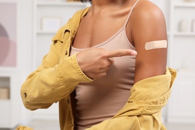 Photo of Young woman pointing at adhesive bandage after vaccination indoors, closeup