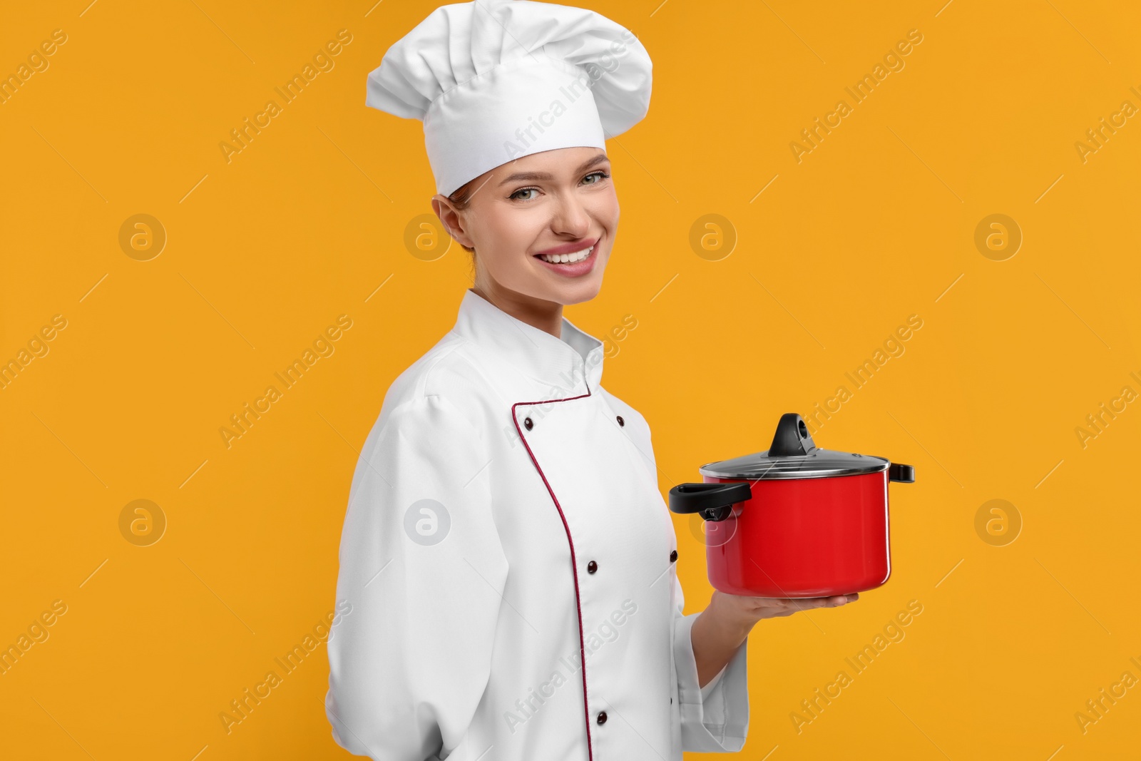 Photo of Happy chef in uniform holding cooking pot on orange background