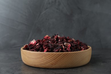 Hibiscus tea. Wooden bowl with dried roselle calyces on grey table, closeup. Space for text