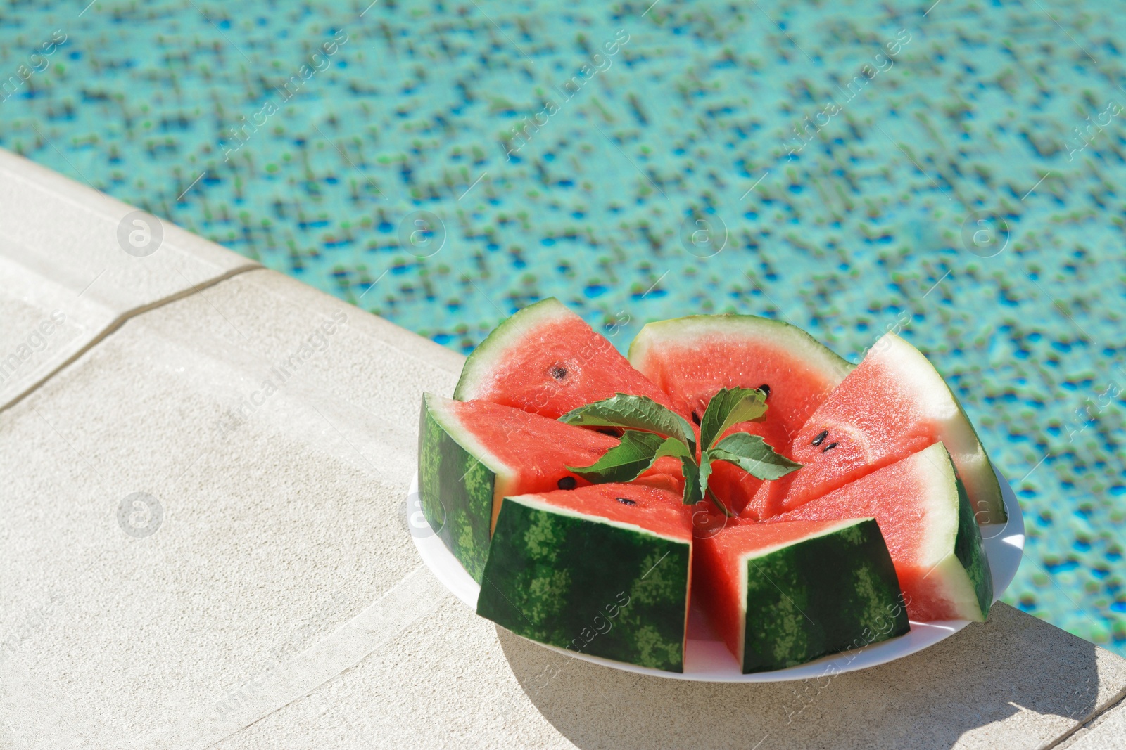 Photo of Slices of watermelon on white plate near swimming pool outdoors. Space for text