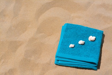Folded soft blue beach towel with seashells on sand, flat lay. Space for text