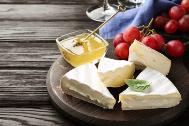 Photo of Tasty brie cheese with basil, grapes and honey on black wooden table