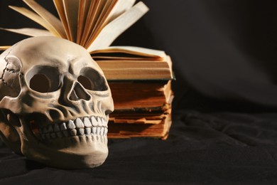 Human skull and old books on black background. Space for text