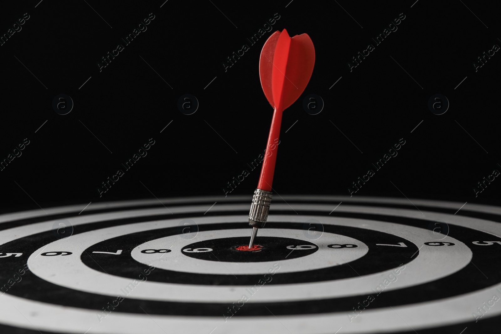 Photo of Red arrow hitting target on dart board against black background