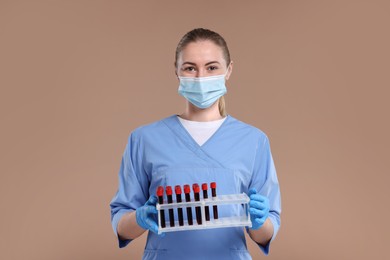 Photo of Laboratory testing. Doctor with blood samples in tubes on light brown background