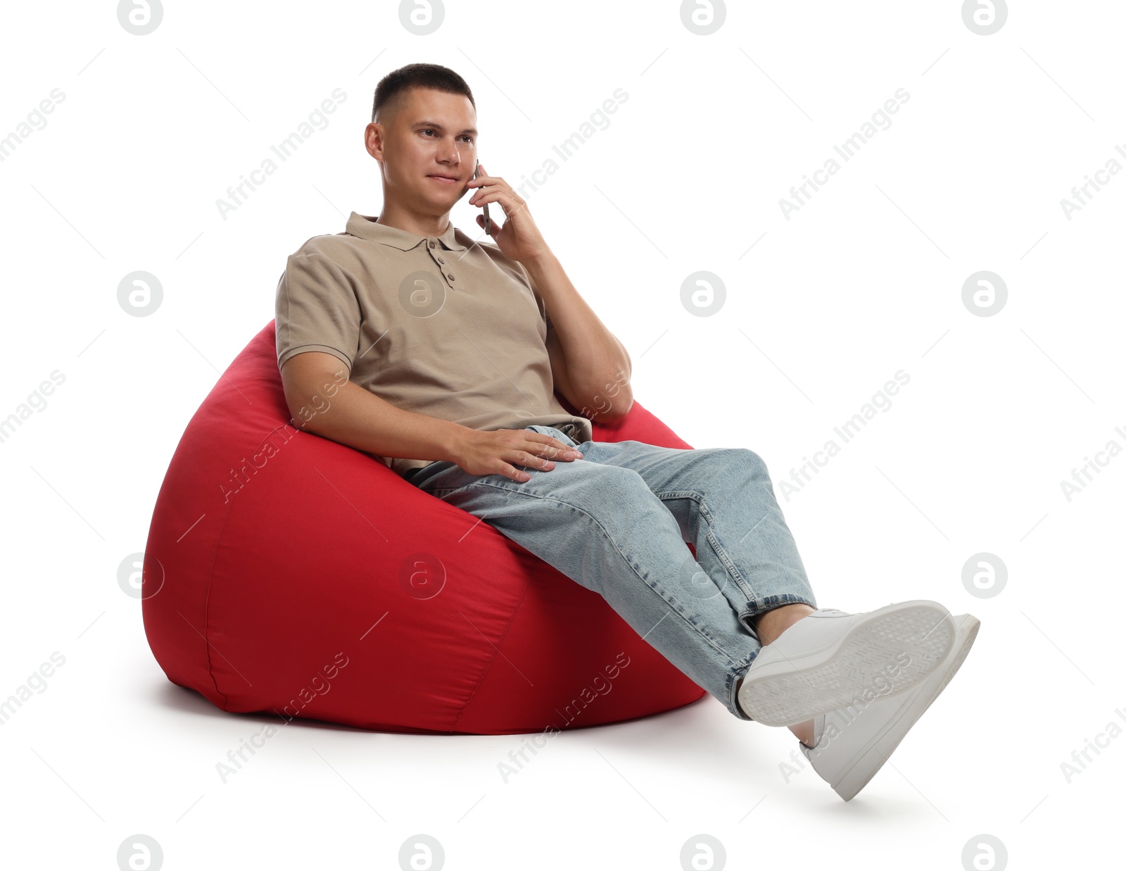 Photo of Handsome man talking by smartphone on red bean bag chair against white background