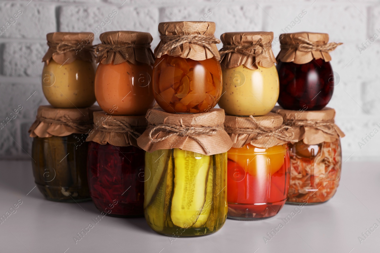 Photo of Many glass jars with different preserved products on light grey table