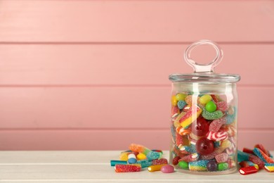 Photo of Jar with different delicious candies on white wooden table against pink background, space for text