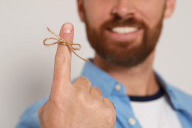 Smiling man showing index finger with tied bow as reminder against light grey background, focus on hand