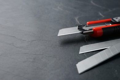 Photo of Utility knife and blades on black table. Space for text