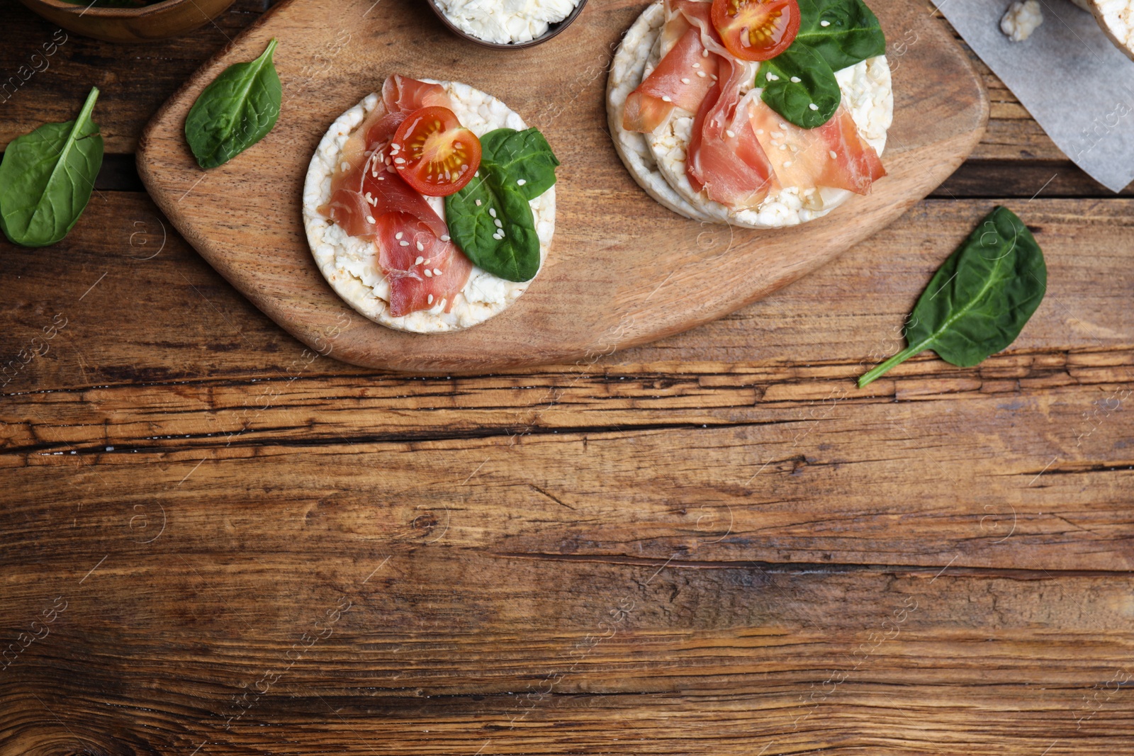 Photo of Puffed rice cakes with prosciutto, tomato and basil on wooden table, flat lay. Space for text