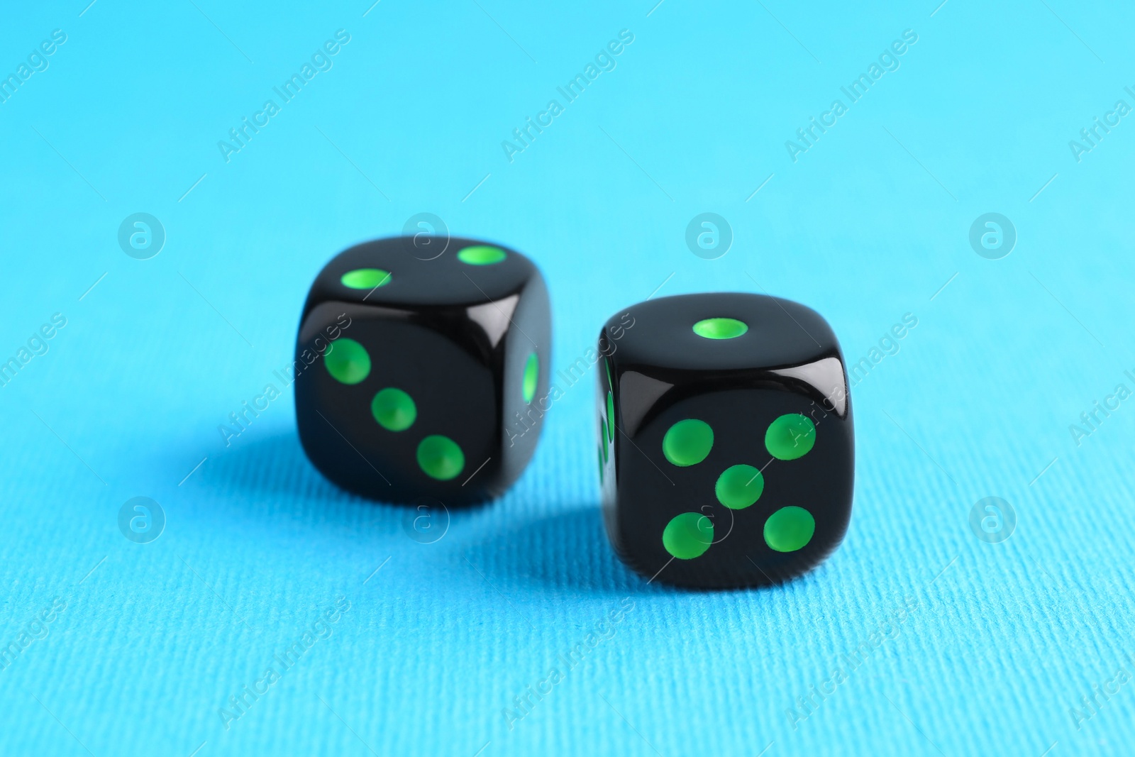 Photo of Two black game dices on light blue background, closeup