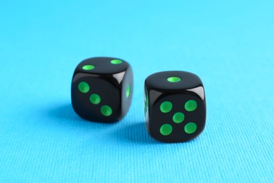 Two black game dices on light blue background, closeup