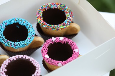 Photo of Box of delicious edible biscuit coffee cups decorated with sprinkles, closeup