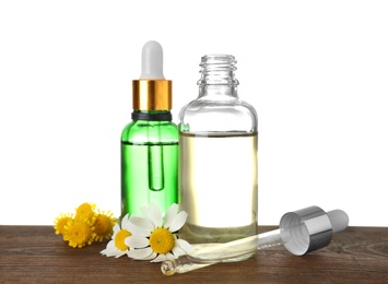 Photo of Bottles of herbal essential oils, pipette and flowers on wooden table, white background