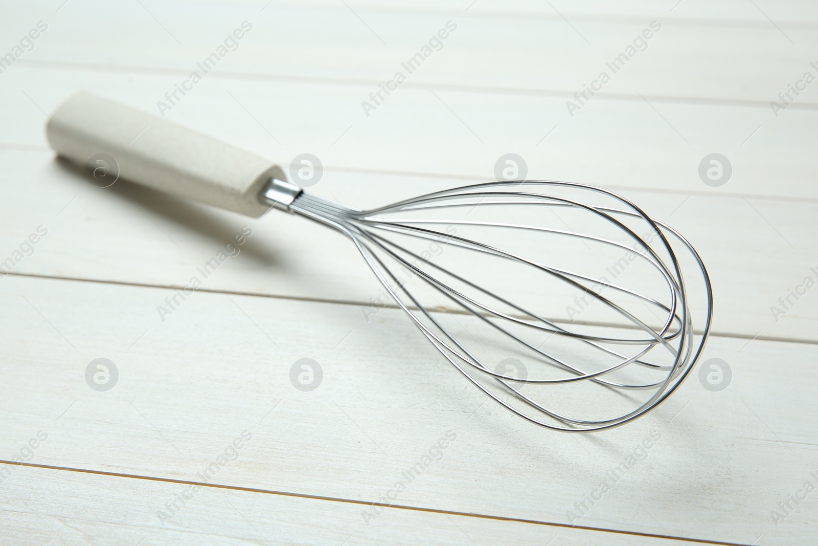 Photo of Metal whisk on white wooden table, closeup