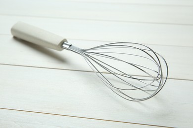 Metal whisk on white wooden table, closeup