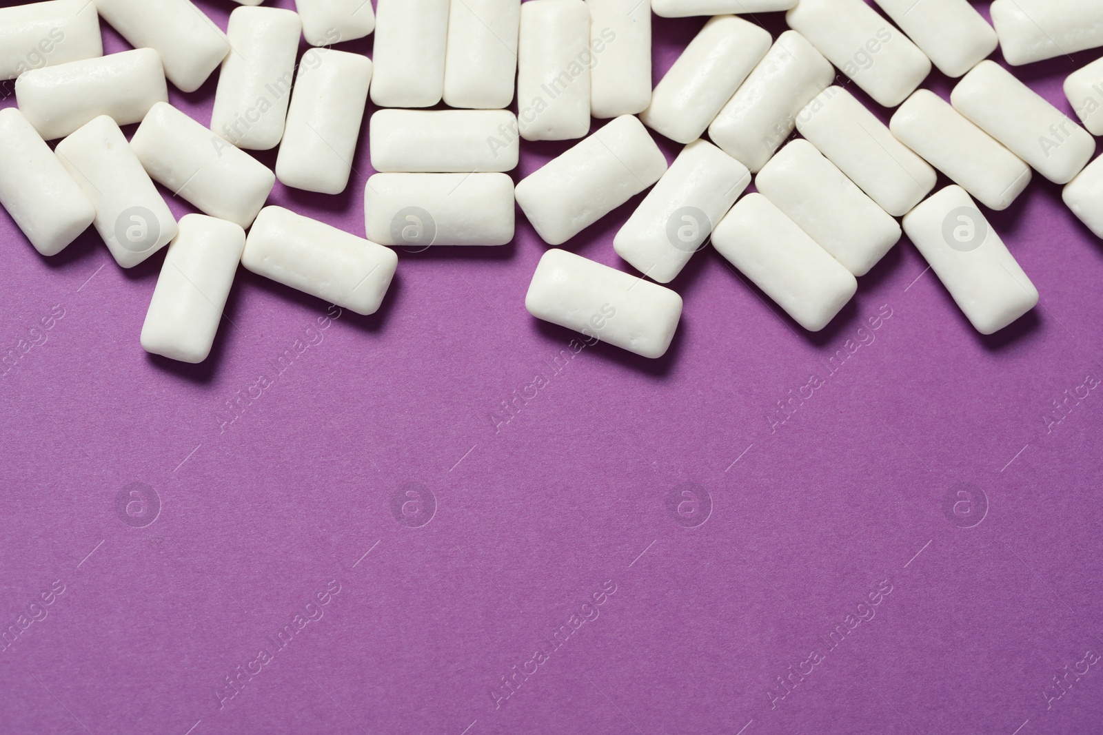 Photo of Tasty white chewing gums on purple background, flat lay. Space for text