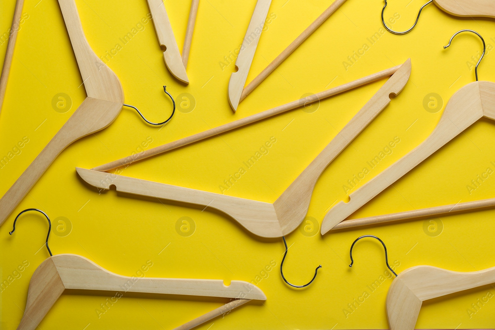 Photo of Wooden hangers on yellow background, flat lay