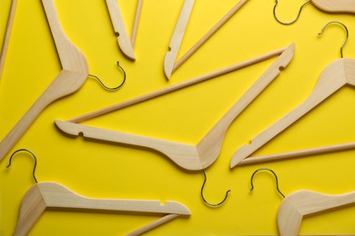 Photo of Wooden hangers on yellow background, flat lay