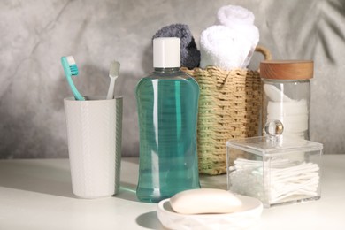 Bottle of mouthwash, toothbrushes and soap on light table in bathroom