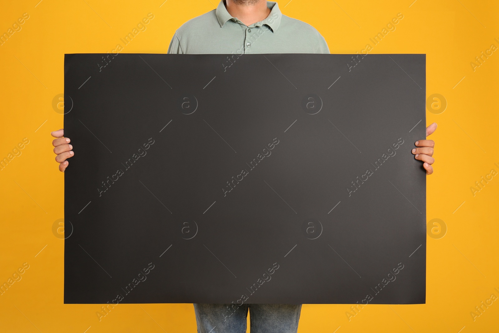 Photo of Man holding black blank poster on yellow background, closeup. Mockup for design