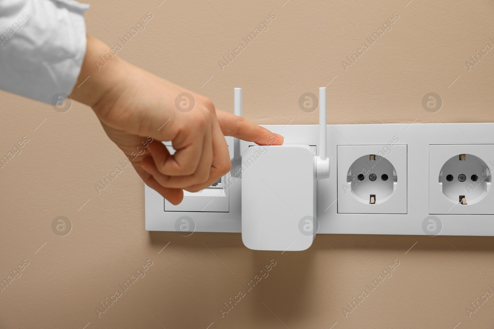 Photo of Woman turning on wireless Wi-Fi repeater indoors, closeup