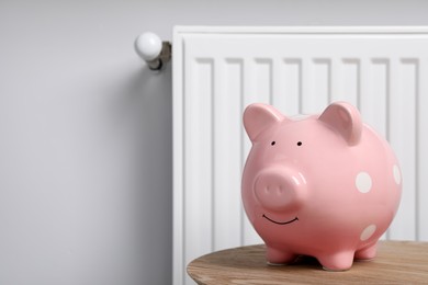 Photo of Piggy bank on wooden table near heating radiator, space for text