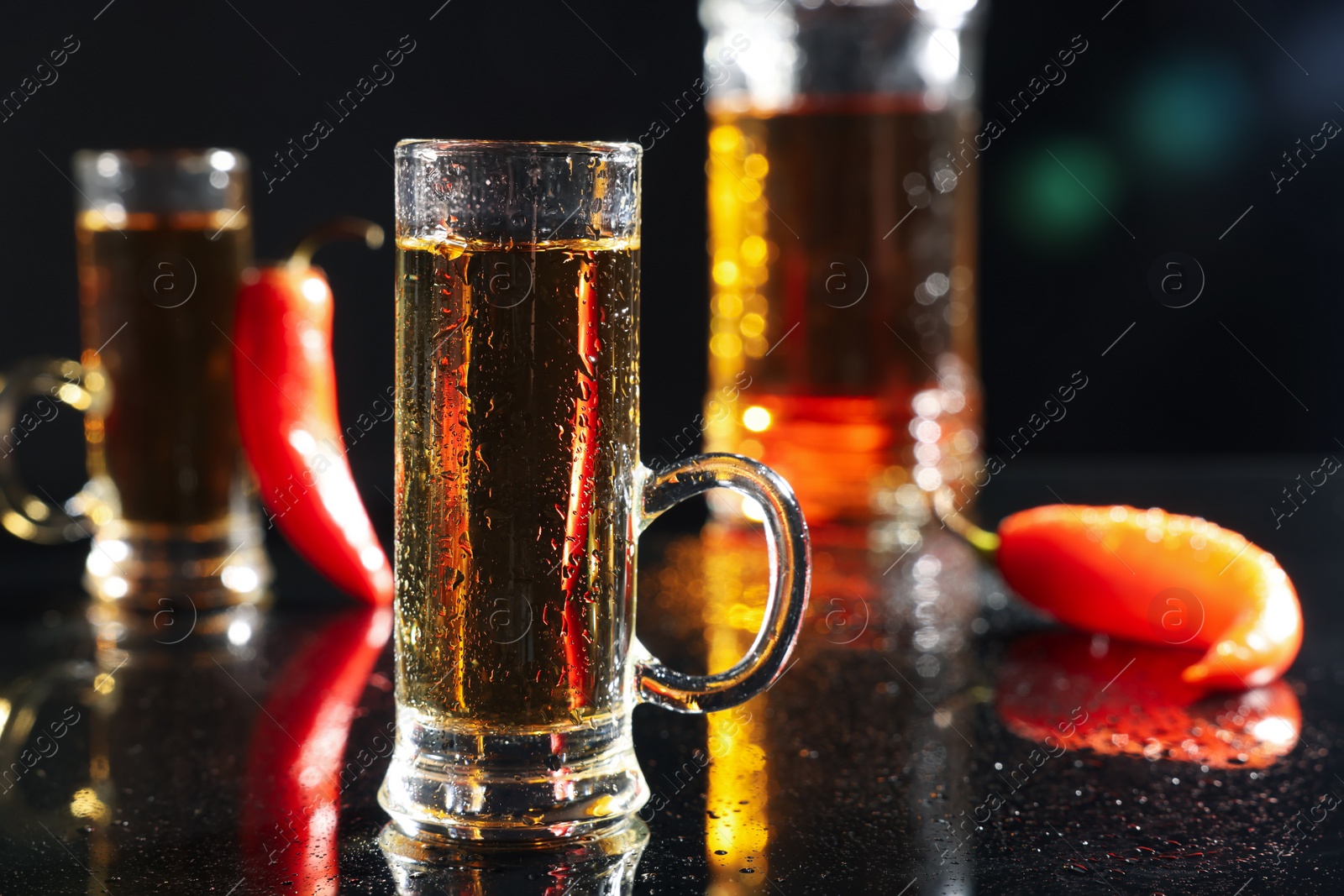 Photo of Red hot chili peppers and vodka on black table, space for text